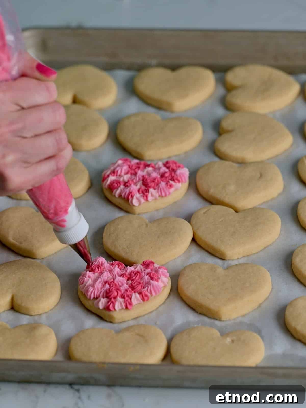 Valentine Sugar Cookies with Creamy Buttercream Frosting 10 Heart cookies being piped with buttercream frosting in shades of pink.
