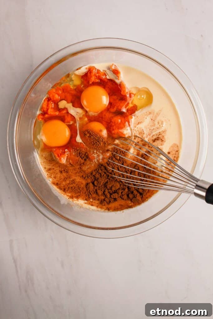 Pumpkin Pecan Dump Cake Recipe — Quick Fall Dessert with Pecans 5 Eggs and pumpkin being mixed in a glass mixing bowl.