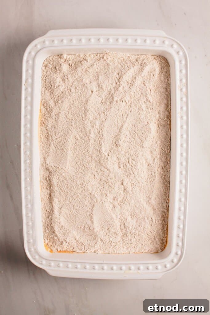Pumpkin Pecan Dump Cake Recipe — Quick Fall Dessert with Pecans 7 Cake mix spread on top of a dessert in a baking dish.