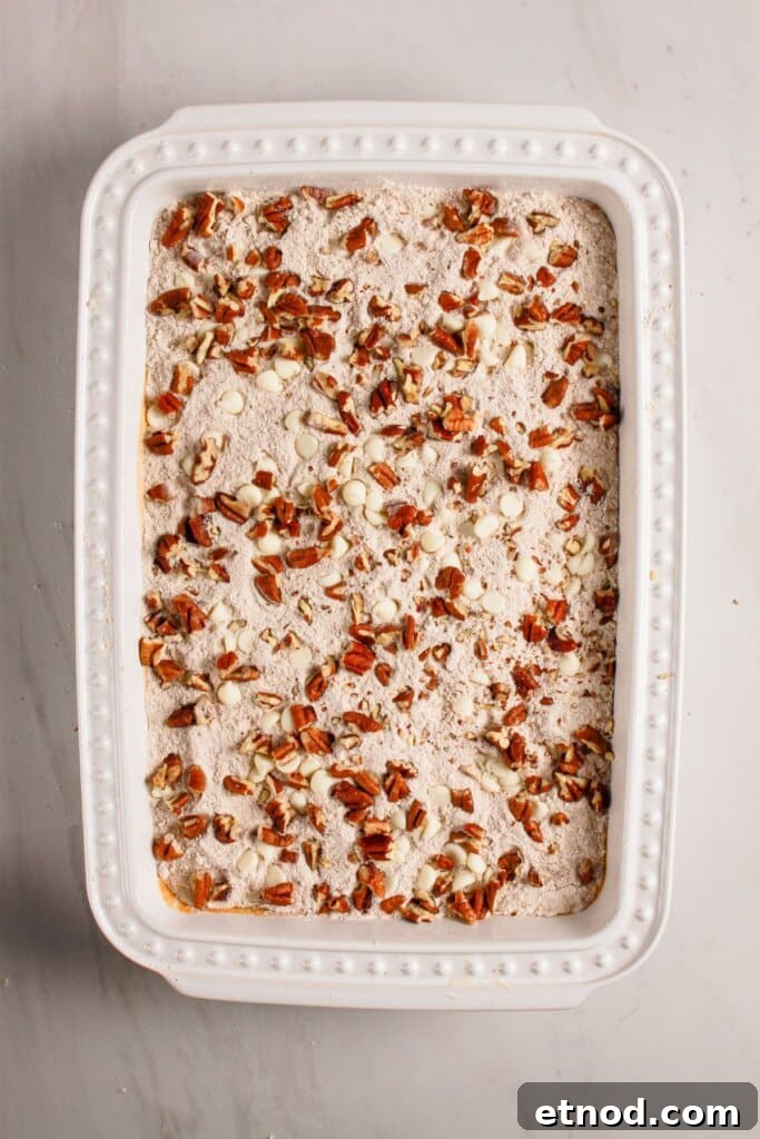 Pumpkin Pecan Dump Cake Recipe — Quick Fall Dessert with Pecans 8 Pecans and white chocolates being sprinkled on top of a dessert.