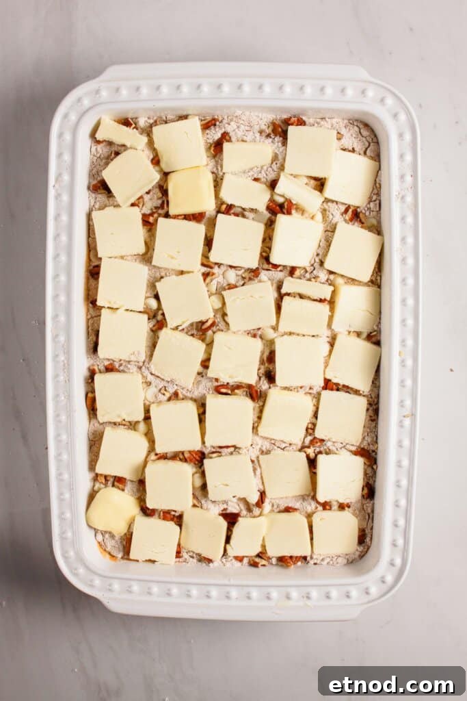 Pumpkin Pecan Dump Cake Recipe — Quick Fall Dessert with Pecans 9 Butter slices being placed on top of a baking dish.