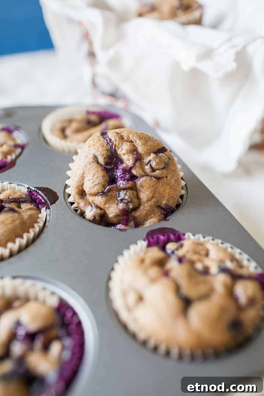 A muffin tray with baked blueberry muffins, one of which is slightly raised, perfect for those make-ahead breakfast recipes.