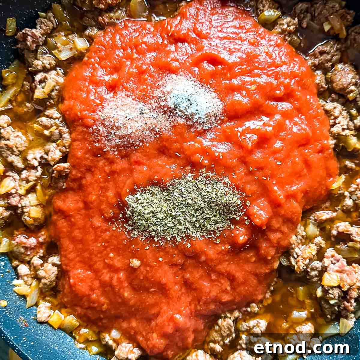 Crushed tomatoes, salt, and Italian spices are added to the lamb mixture in the frying pan.