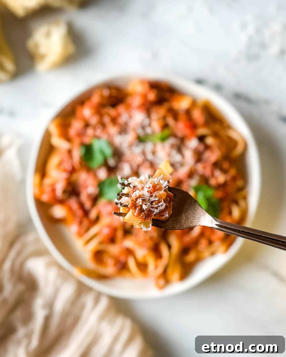 Closeup of pappardelle pasta twirled on a forked and coated with lamb ragu over a plate of slow cooker lamb ragu.