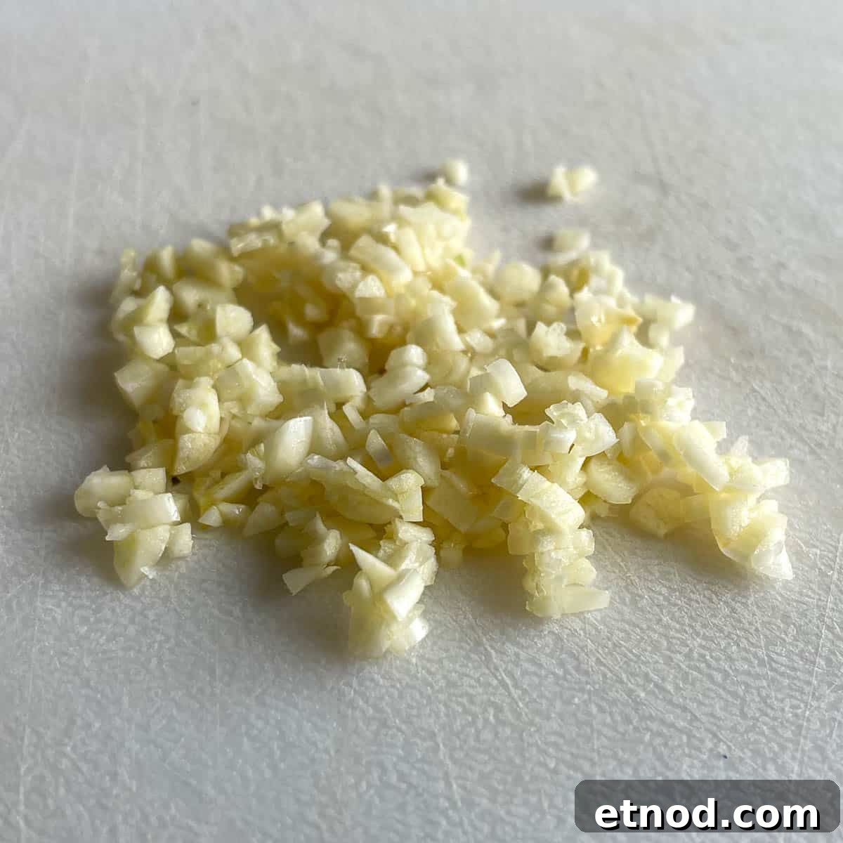 Minced garlic sits on a white cutting board.