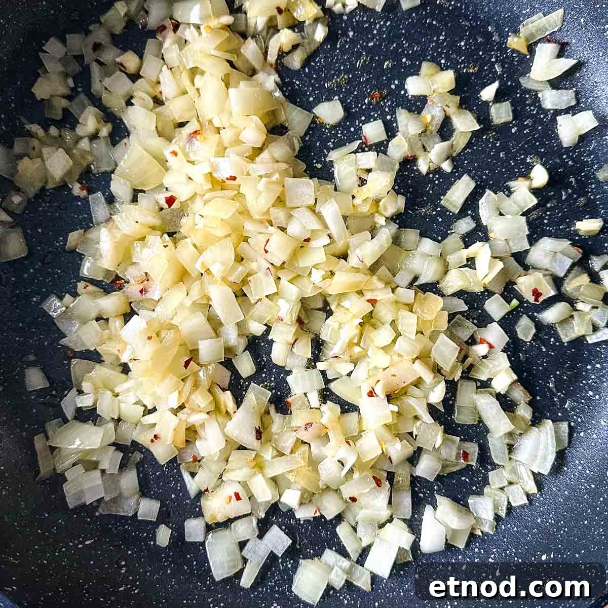 garlic and chili flakes are added to the onion sweating in a frying pan.
