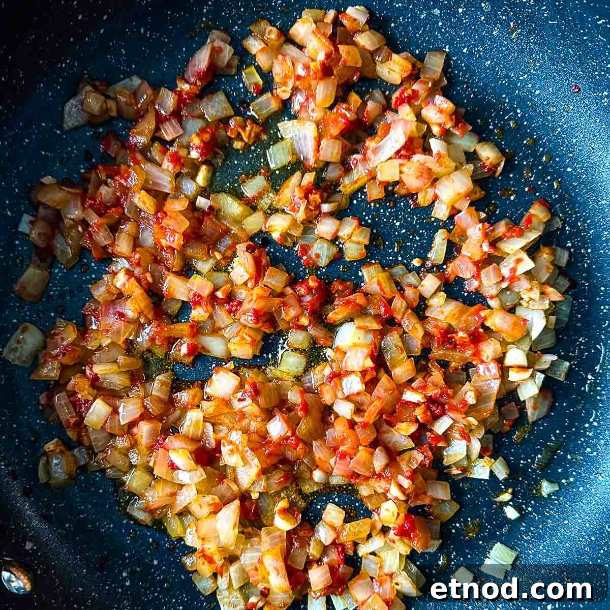 cooked down tomato paste in a gray frying pan with sweated onion, garlic, and chili flakes.