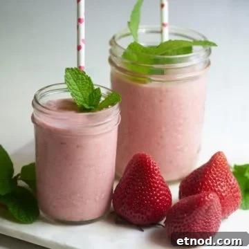 Two strawberry dairy-free milkshakes with straws and sprigs of mint on a tray with fresh strawberries.