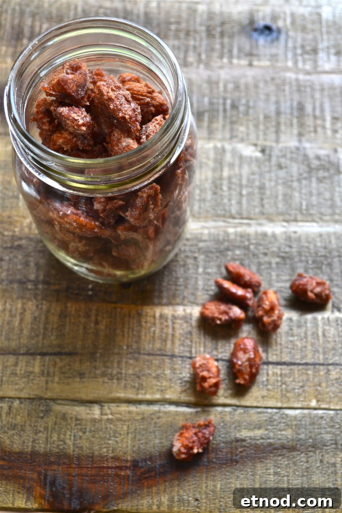 How to Make Irresistible Candied Almonds at Home 2 A glass jar filled with candied pecans and candied almonds sits on a rustic wooden surface, with several sugared pecans scattered beside the jar.