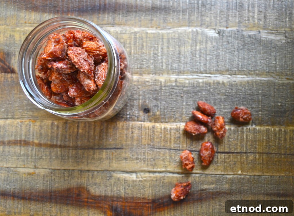 How to Make Irresistible Candied Almonds at Home 3 A glass jar filled with sweet candied almonds sits on a wooden surface, with a few candied almonds scattered beside the jar.