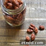 How to Make Irresistible Candied Almonds at Home 4 A glass jar filled with candied pecans and candied almonds sits on a rustic wooden surface, with several sugared pecans scattered beside the jar.