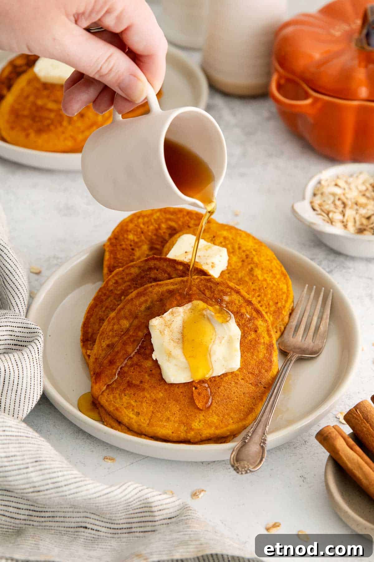 three oat flour pumpkin pancakes with butter and syrup being poured on.