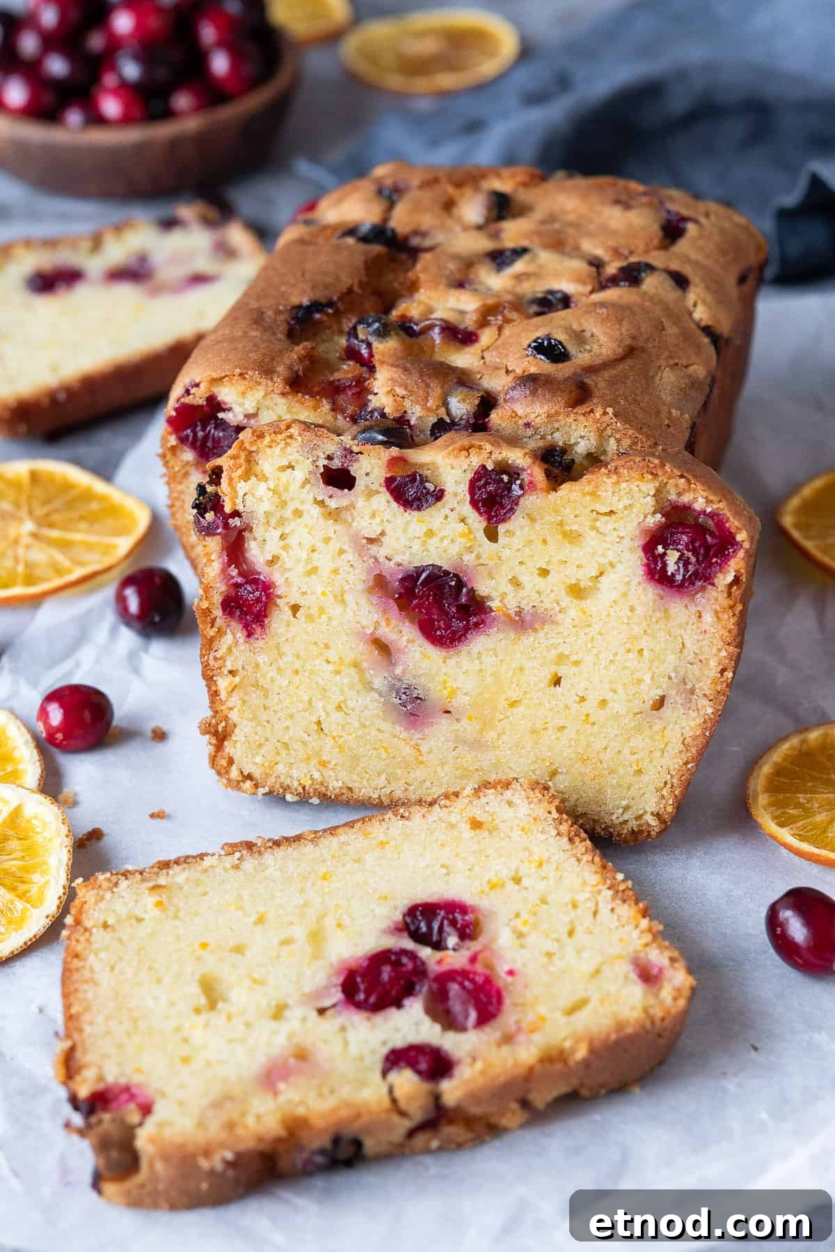 Vegan orange cranberry cake slices. Vegan orange cranberry cake with three slices cut with dried orange slices and a bowl of fresh cranberries in the background.
