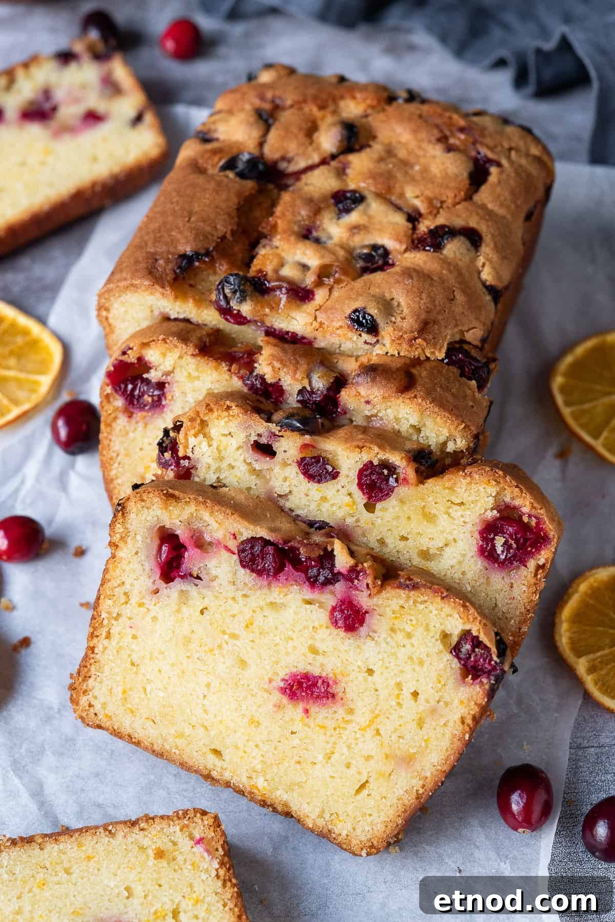 Sliced vegan orange cranberry bread. Sliced cranberry orange bread on a sheet of baking parchment on a grey background.