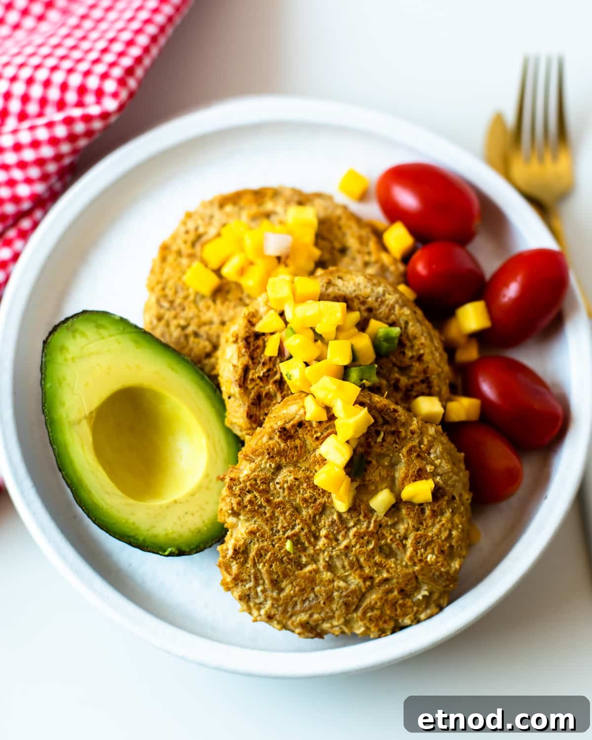 Easy 4 ingredient tuna patties with mango salsa, cherry tomatoes, and avocado served on a white plate with gold fork.