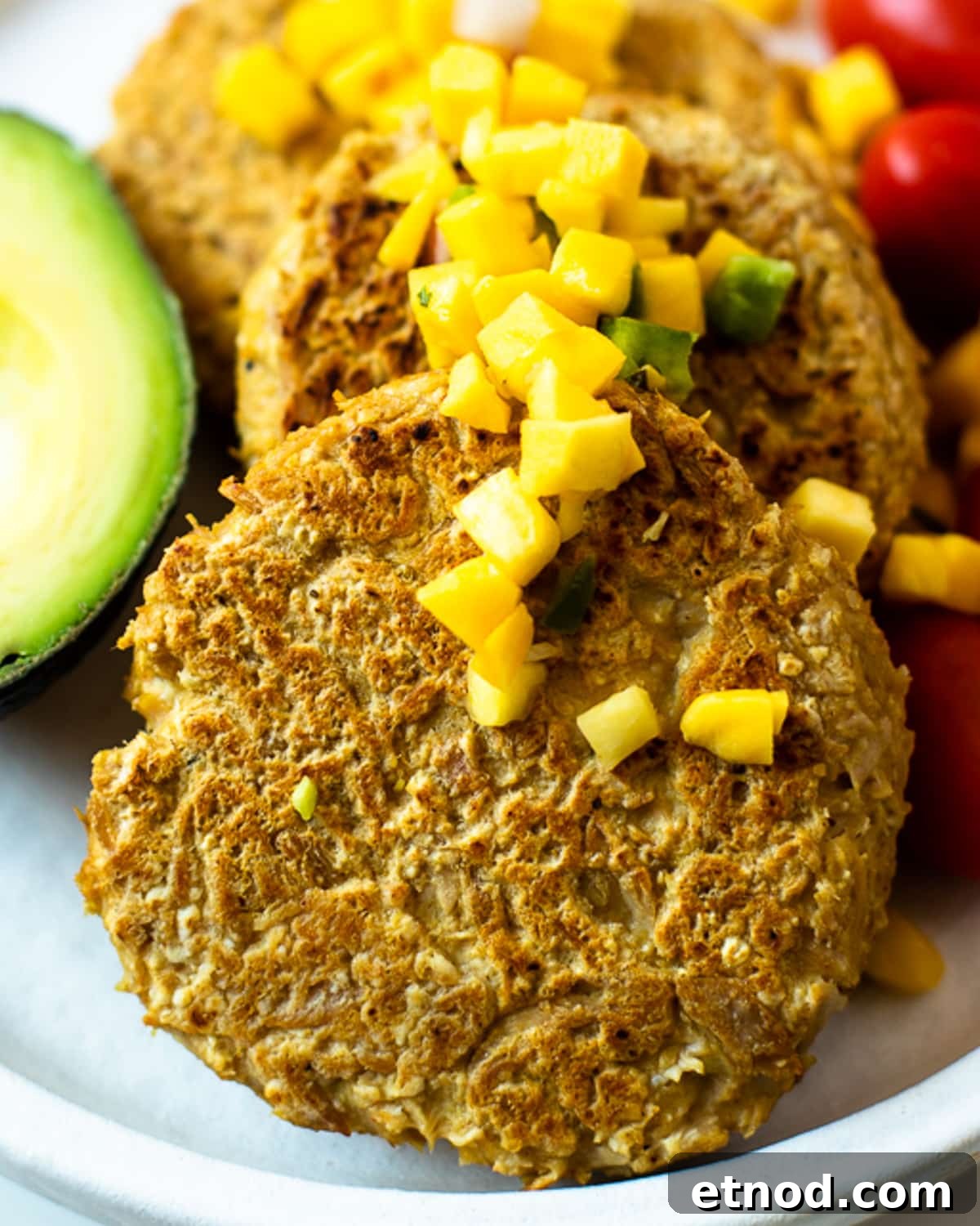 Close-up of crispy golden brown tuna patty topped with fresh mango salsa, showing texture and firm interior.