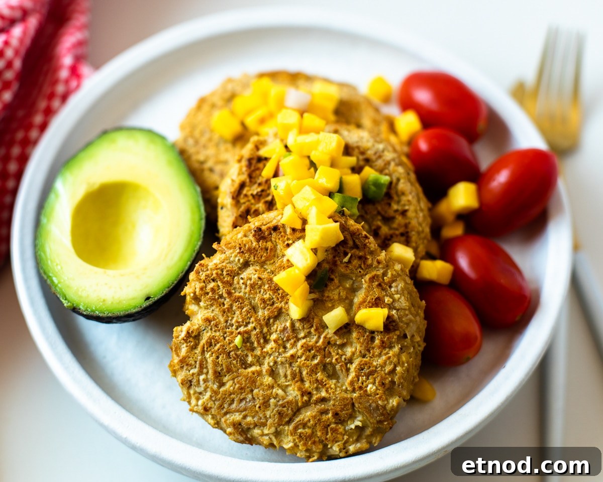Gluten-free 4 ingredient tuna patties topped with mango avocado salsa, served with cherry tomatoes and half an avocado on a white plate.