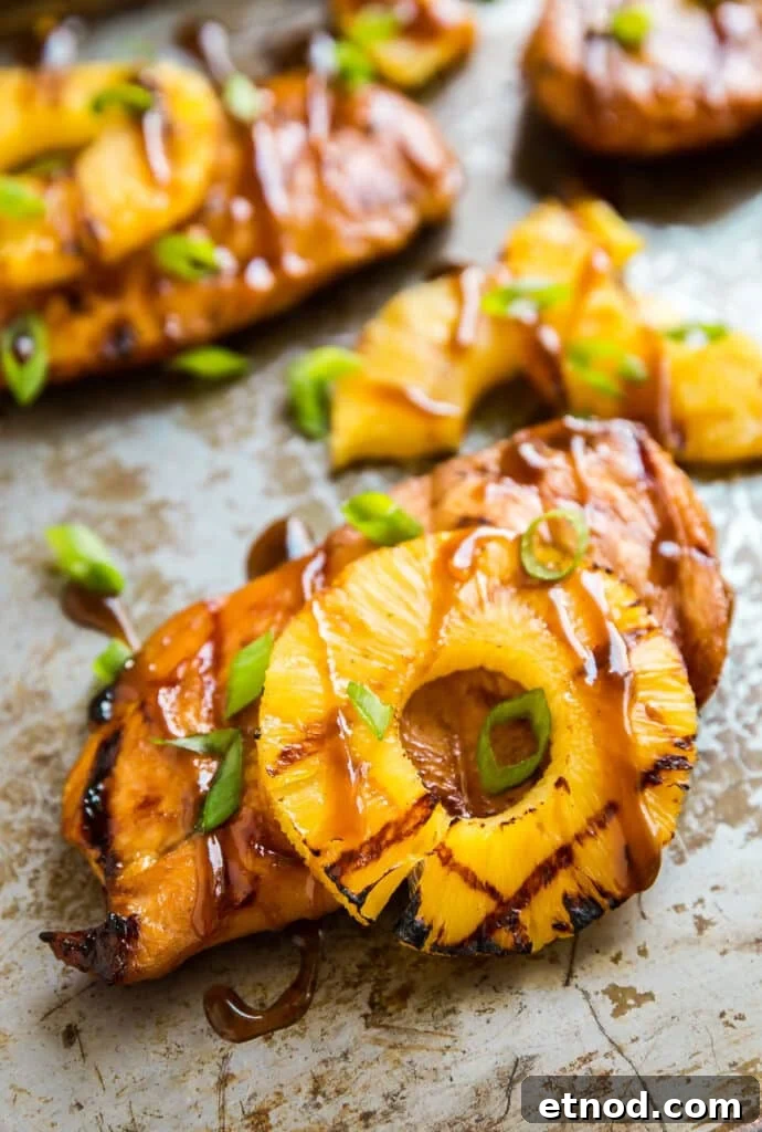 Hawaiian Aloha Chicken Recipe with Pineapple and Teriyaki Glaze 2 a Piece of pineapple chicken breast with a grilled pineapple slice on a pan with other pieces behind it.