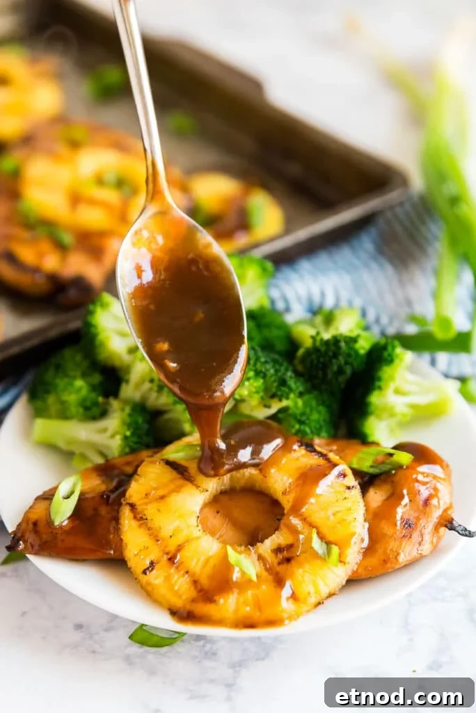 Hawaiian Aloha Chicken Recipe with Pineapple and Teriyaki Glaze 8 A side angle image of hawaiian chicken and pineapple on a plate with sauce being drizzled on top with a spoon.