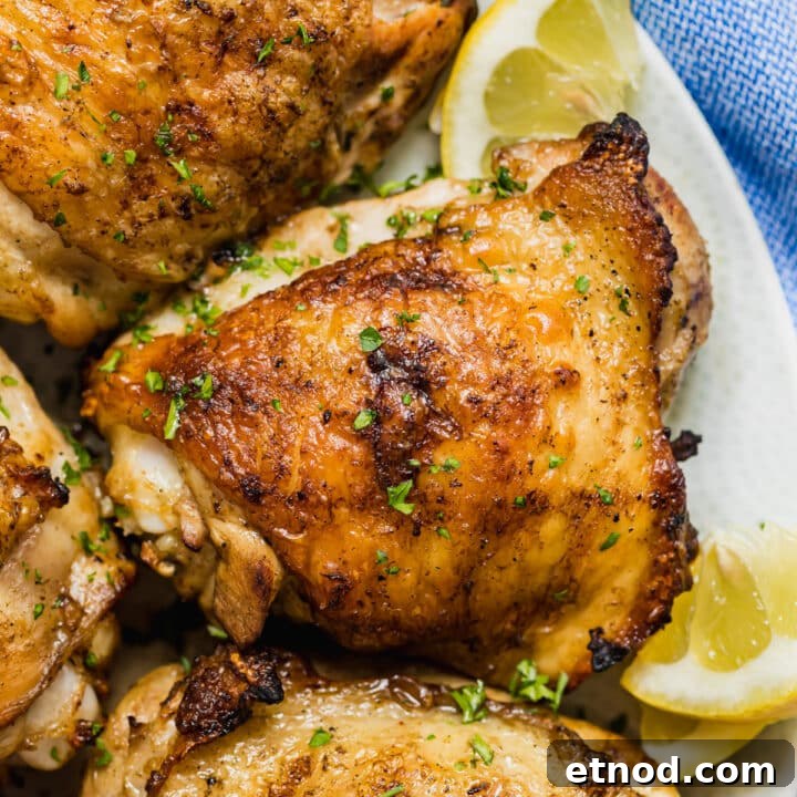 A close up overhead image of grilled chicken thighs on a plate with lemons.