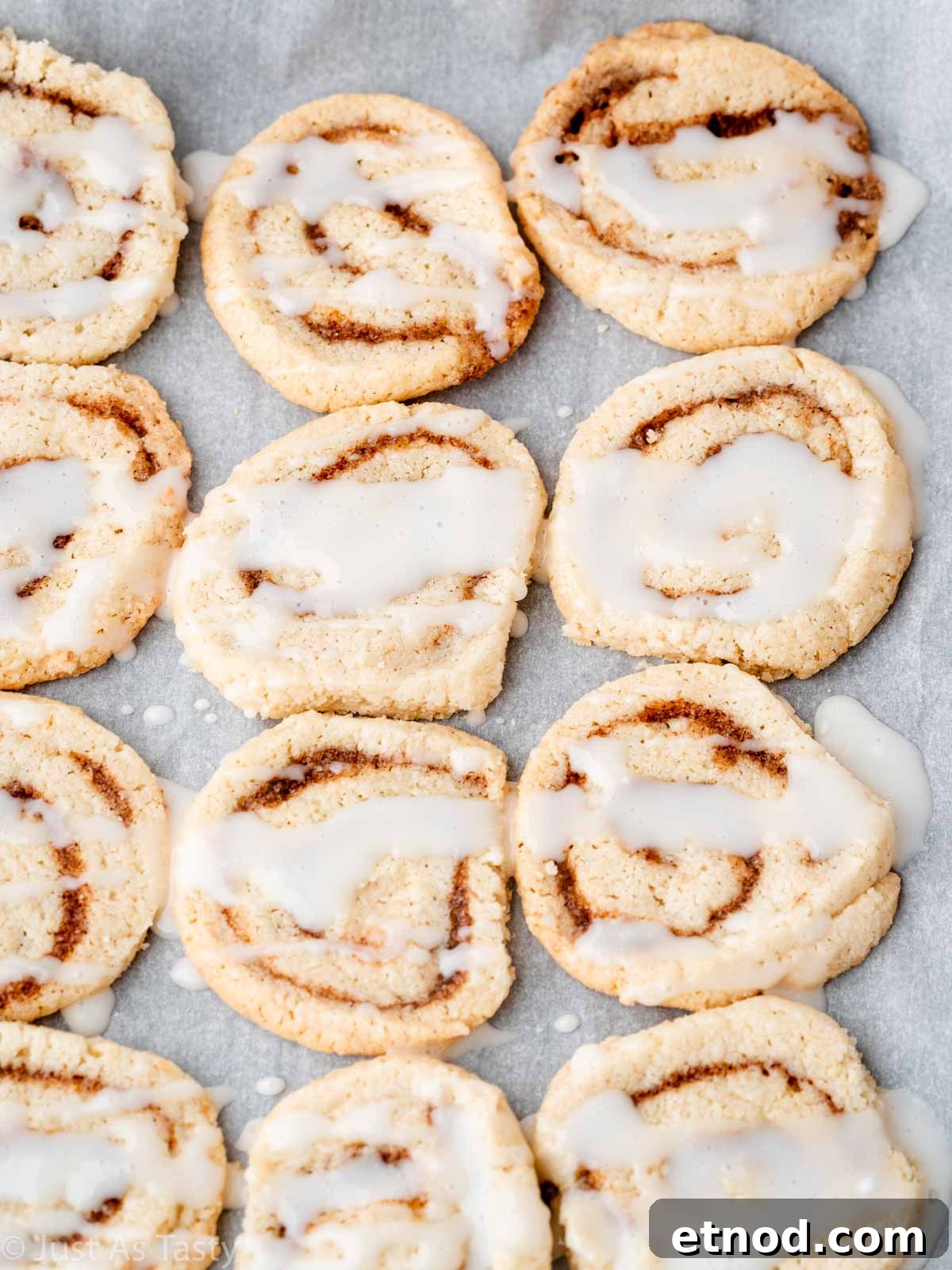 Glazed cinnamon roll cookies lined up on parchment paper. 