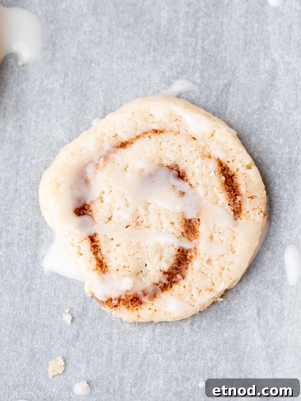 Close-up of a glazed cinnamon roll cookie on parchment paper. 