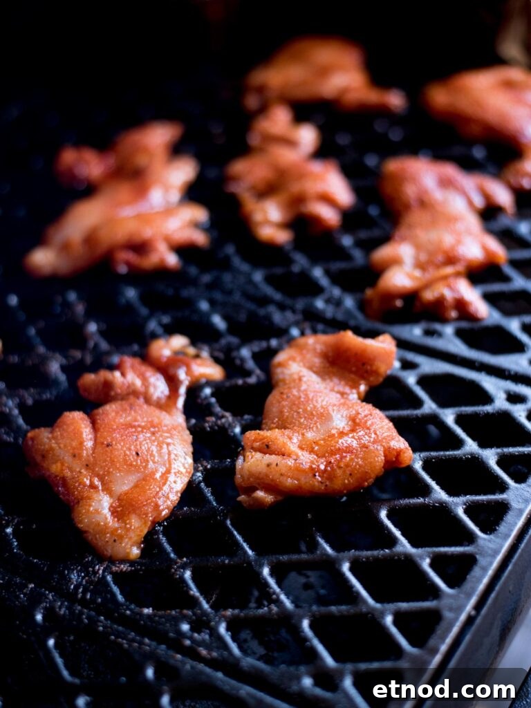 Juicy Chicken Thighs on a Pellet Grill: Flavorful Recipe Guide 6 Raw seasoned chicken thighs laying on the grate of a smoker.