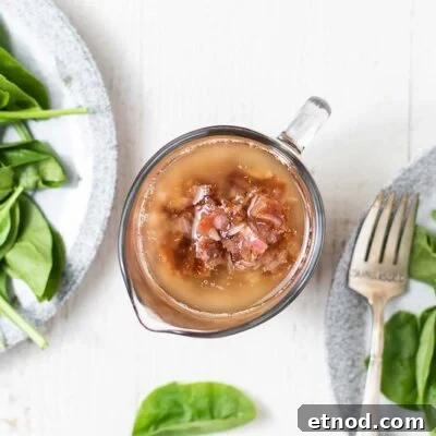 A dressing container filled with hot bacon dressing sitting next to a spinach salad.