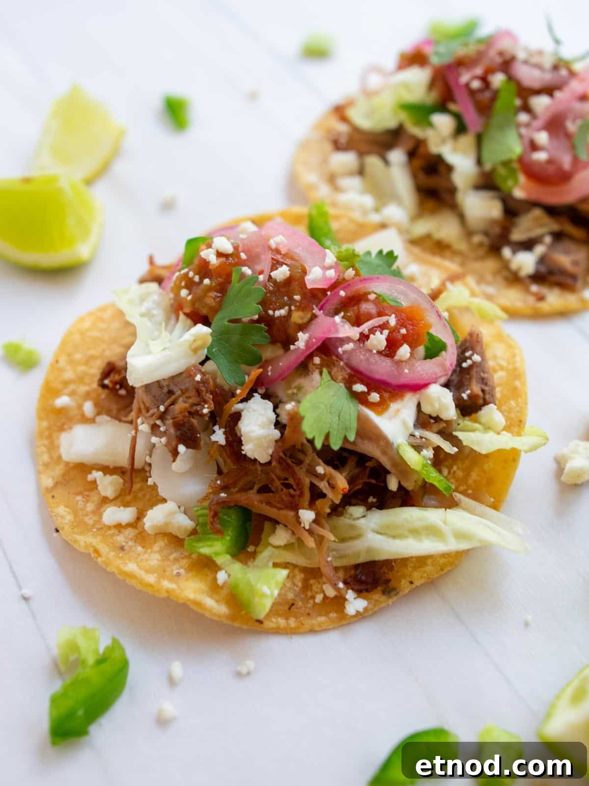 Crispy Instant Pot Carnitas Recipe for Authentic Mexican Flavor 2 Instant pot carnitas tacos on a white background with limes on the side.