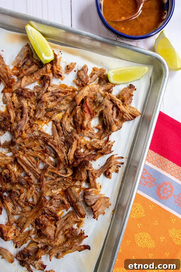 Crispy Instant Pot Carnitas Recipe for Authentic Mexican Flavor 9 Broiled carnitas meat on tray with extra sauce and limes.