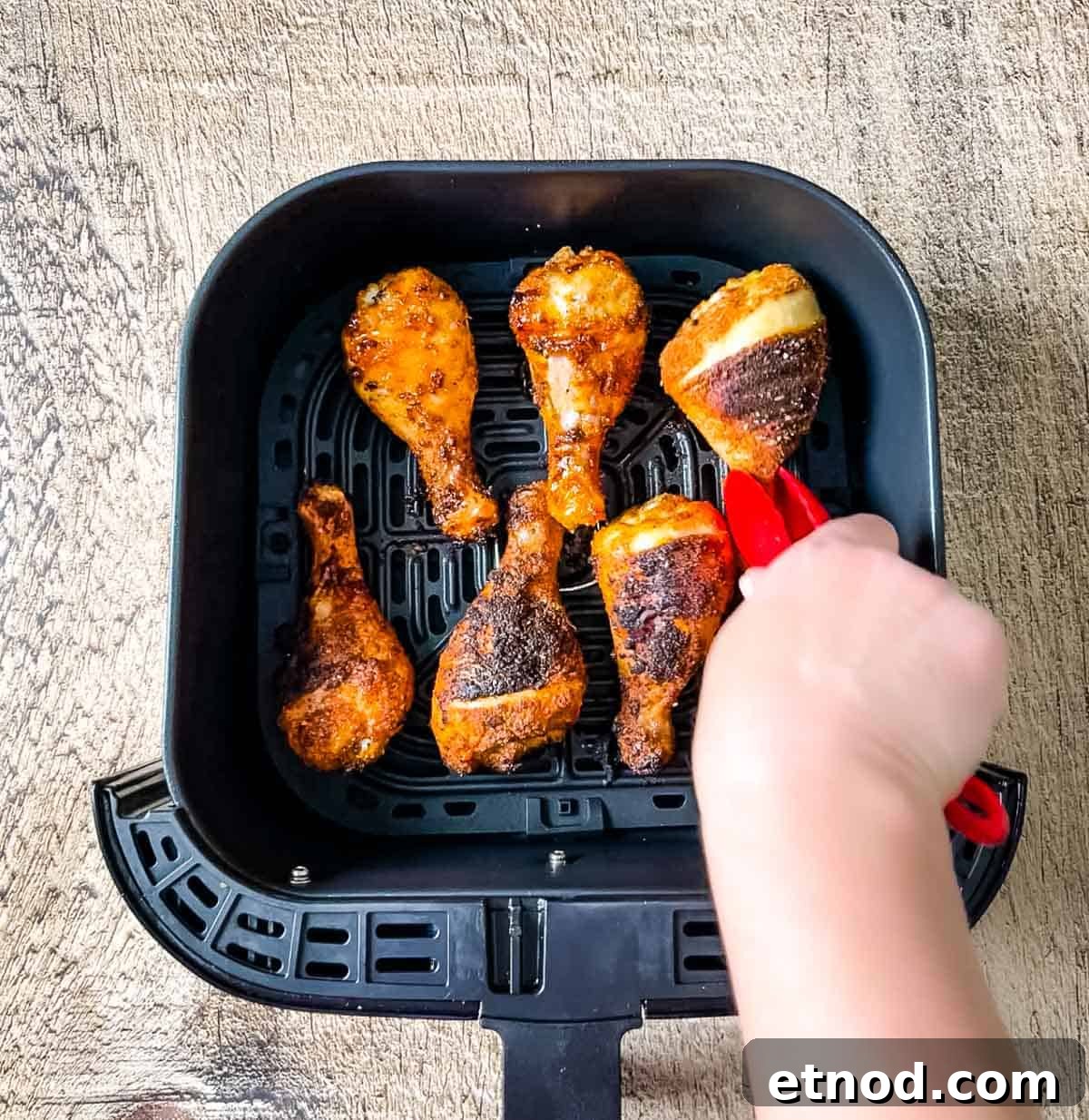 Crispy Air Fryer Chicken Drumsticks — Quick Weeknight Recipe 11 A hand using tongs to flip the chicken legs over in the air fryer basket.