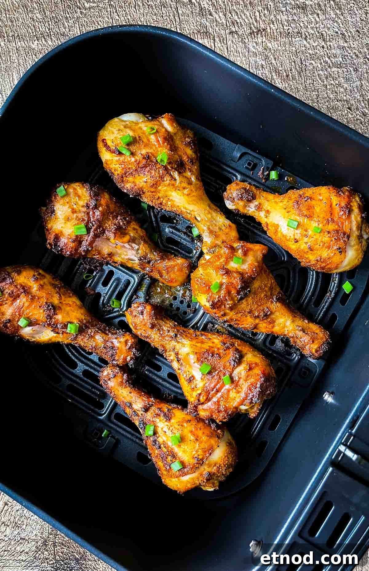 Crispy Air Fryer Chicken Drumsticks — Quick Weeknight Recipe 13 A closeup of chicken legs in the air fryer basket, topped with green onion for garnish.