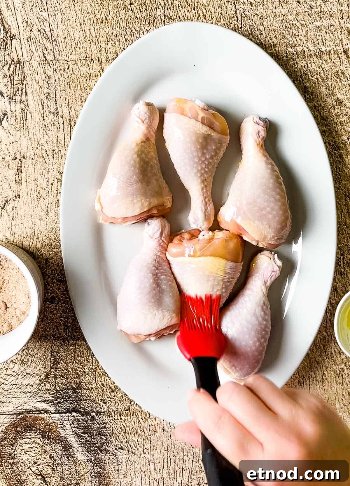 Crispy Air Fryer Chicken Drumsticks — Quick Weeknight Recipe 5 A hand brushing the chicken legs with olive oil.
