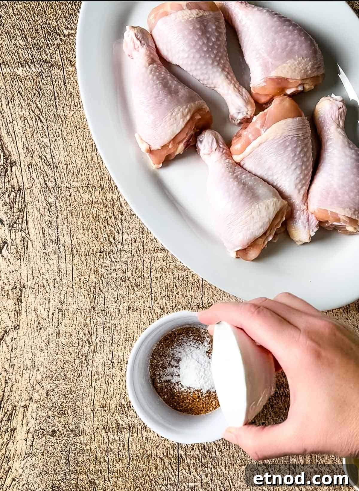 Crispy Air Fryer Chicken Drumsticks — Quick Weeknight Recipe 6 A hand pouring baking powder into the dry rub mixture in a white bowl.