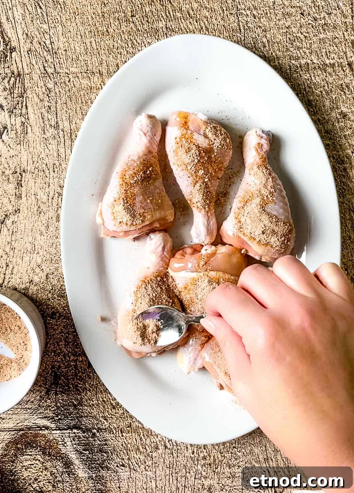 Crispy Air Fryer Chicken Drumsticks — Quick Weeknight Recipe 8 A hand using a spoon to sprinkle spice rub onto the chicken legs.