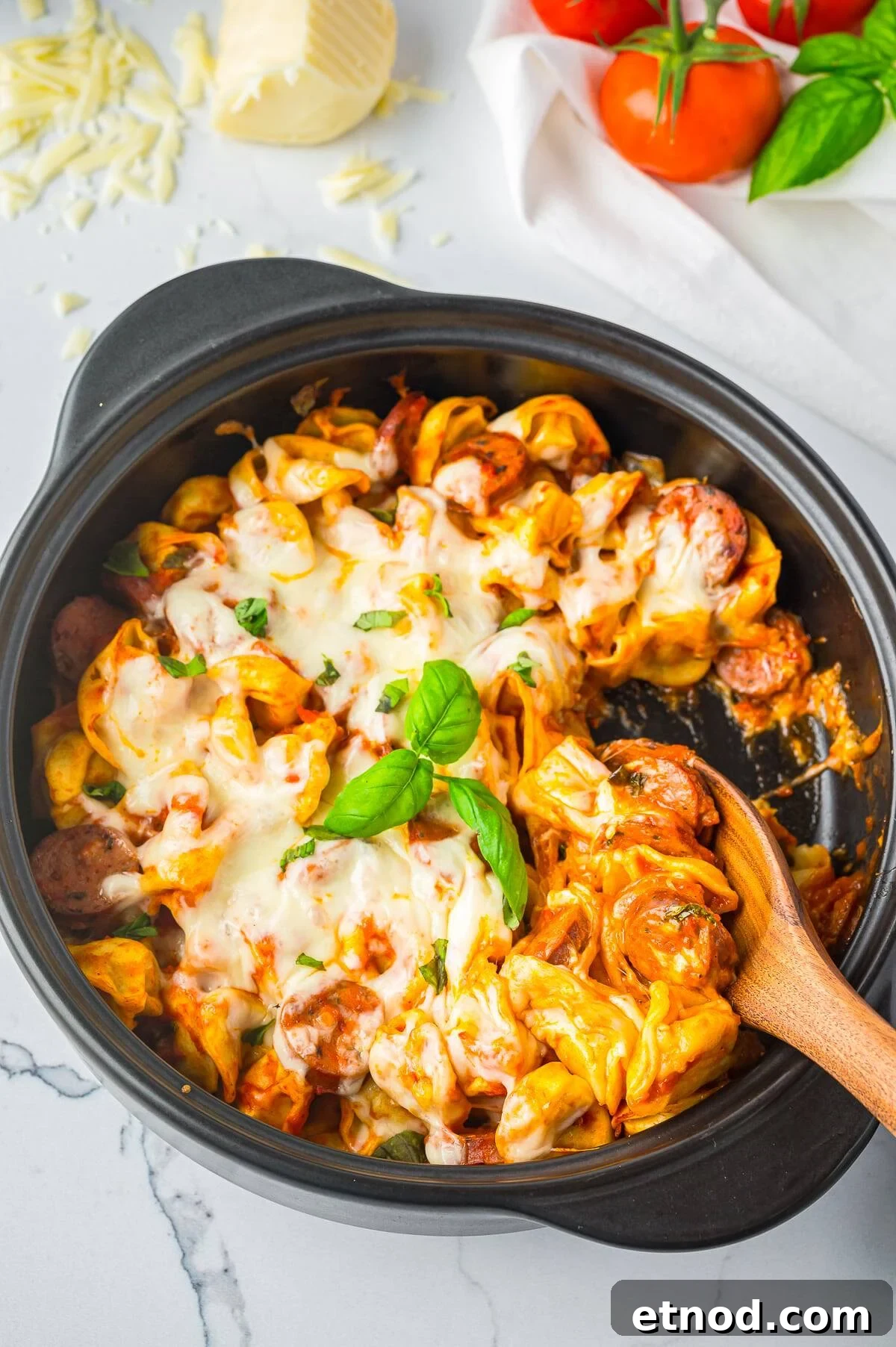 Creamy Italian Sausage Tortellini Bake: Cheesy Oven Pasta Delight 2 Sausage tortellini bake in a black skillet topped with melted mozzarella and fresh basil.