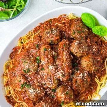 Spaghetti and Meatballs with Italian sausage served on a platter with basil and parmesan.
