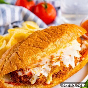 Chicken parmesan sandwich on a hoagie roll with melted mozzarella and marinara on a plate.