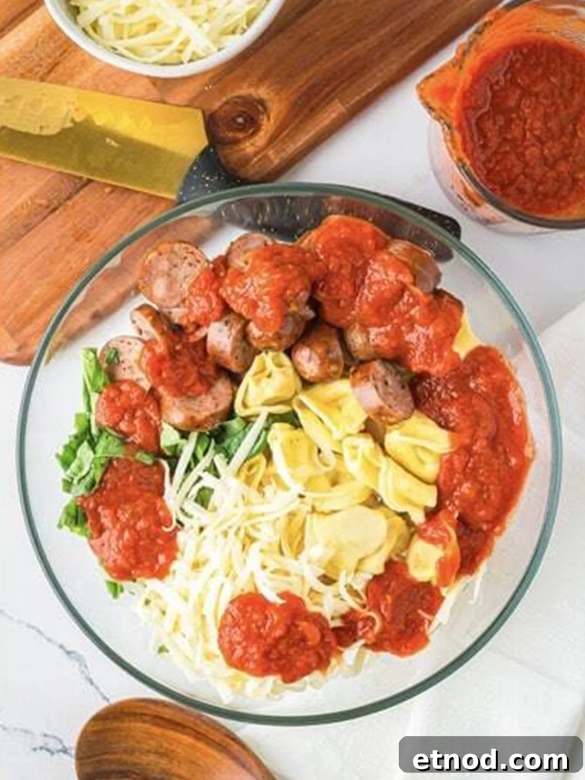 Creamy Italian Sausage Tortellini Bake: Cheesy Oven Pasta Delight 6 Tortellini, sliced sausage, marinara, mozzarella, and basil combined in a large mixing bowl.