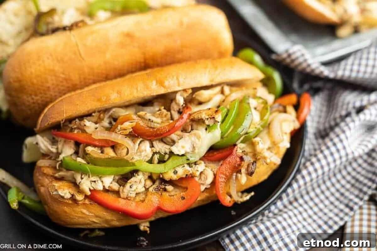 Blackstone Philly Cheesesteak Chicken Sandwich Recipe 2 Blackstone Chicken Philly Cheesesteak, filled with shredded grilled chicken, sautéed green and red bell peppers, and onions on a toasted hoagie roll, served on a black plate.