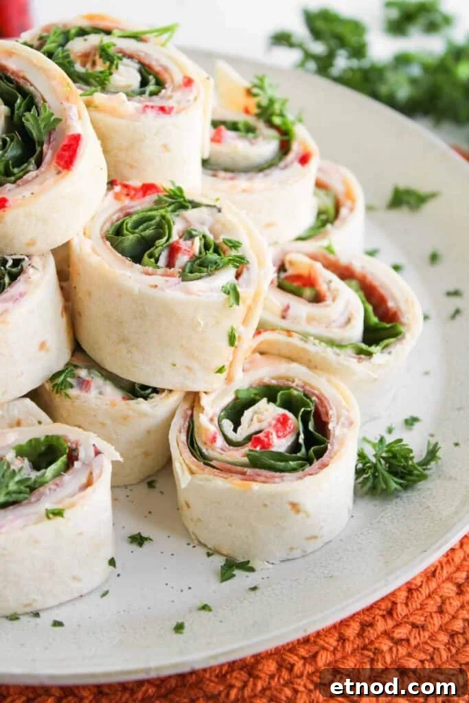 A plate of Italian Sub Pinwheels with visible layers of deli meat, cheese, leafy greens, and red peppers, garnished with chopped parsley.
