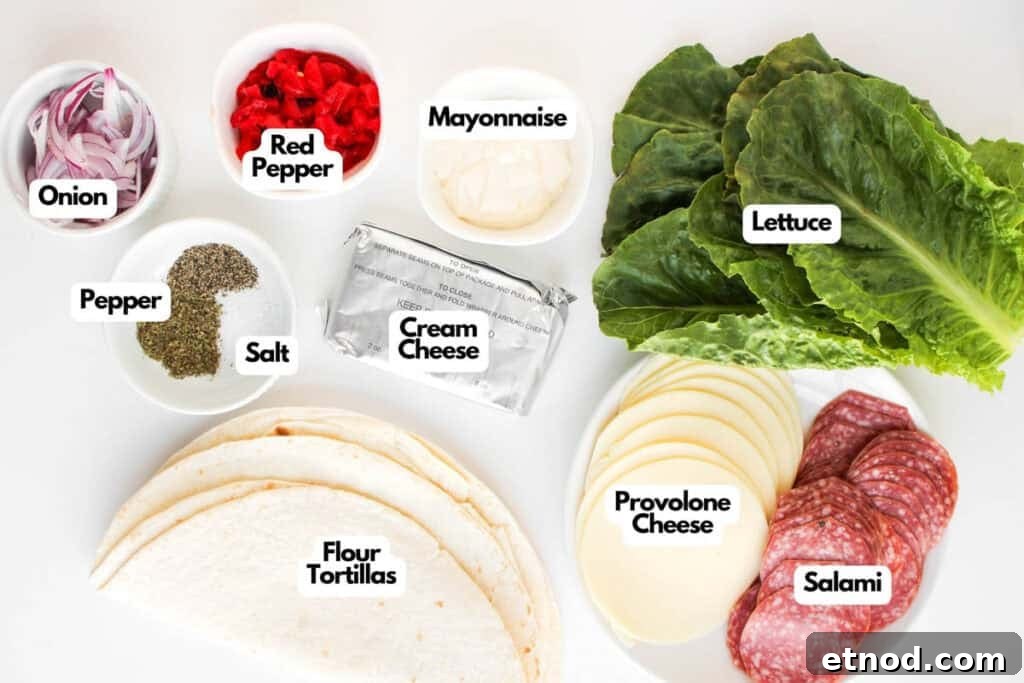 Assorted sandwich ingredients for Italian Sub Pinwheels, including onion, red pepper, mayonnaise, lettuce, cream cheese, provolone cheese, salami, flour tortillas, salt, and pepper arranged on a white surface.