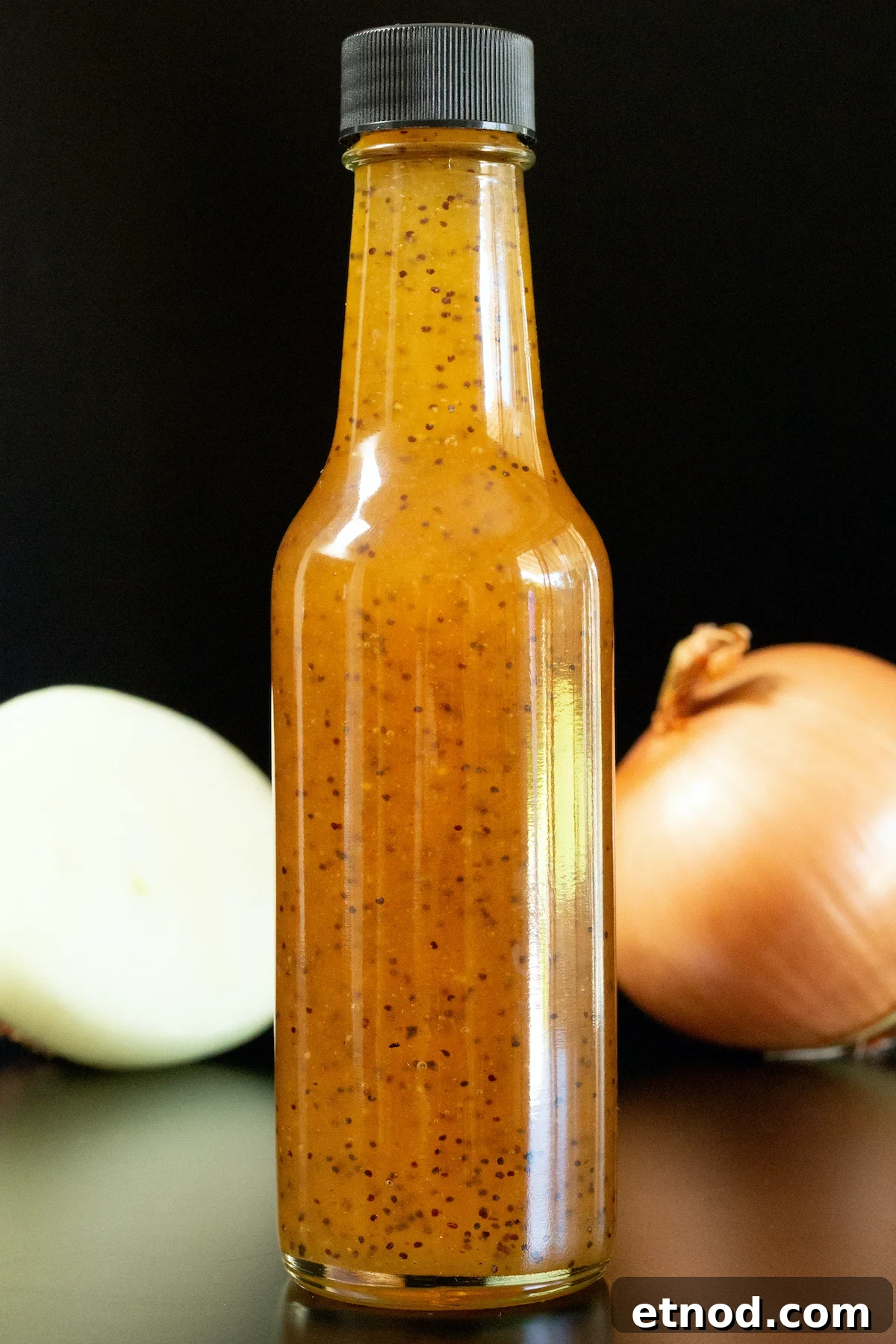 Subway Sweet Onion Sauce: Flavor, Ingredients & How It's Made 2 A small glass bottle filled with brown copycat subway sweet onion sauce is in focus. A sliced and unsliced onion are out of focus in the background.