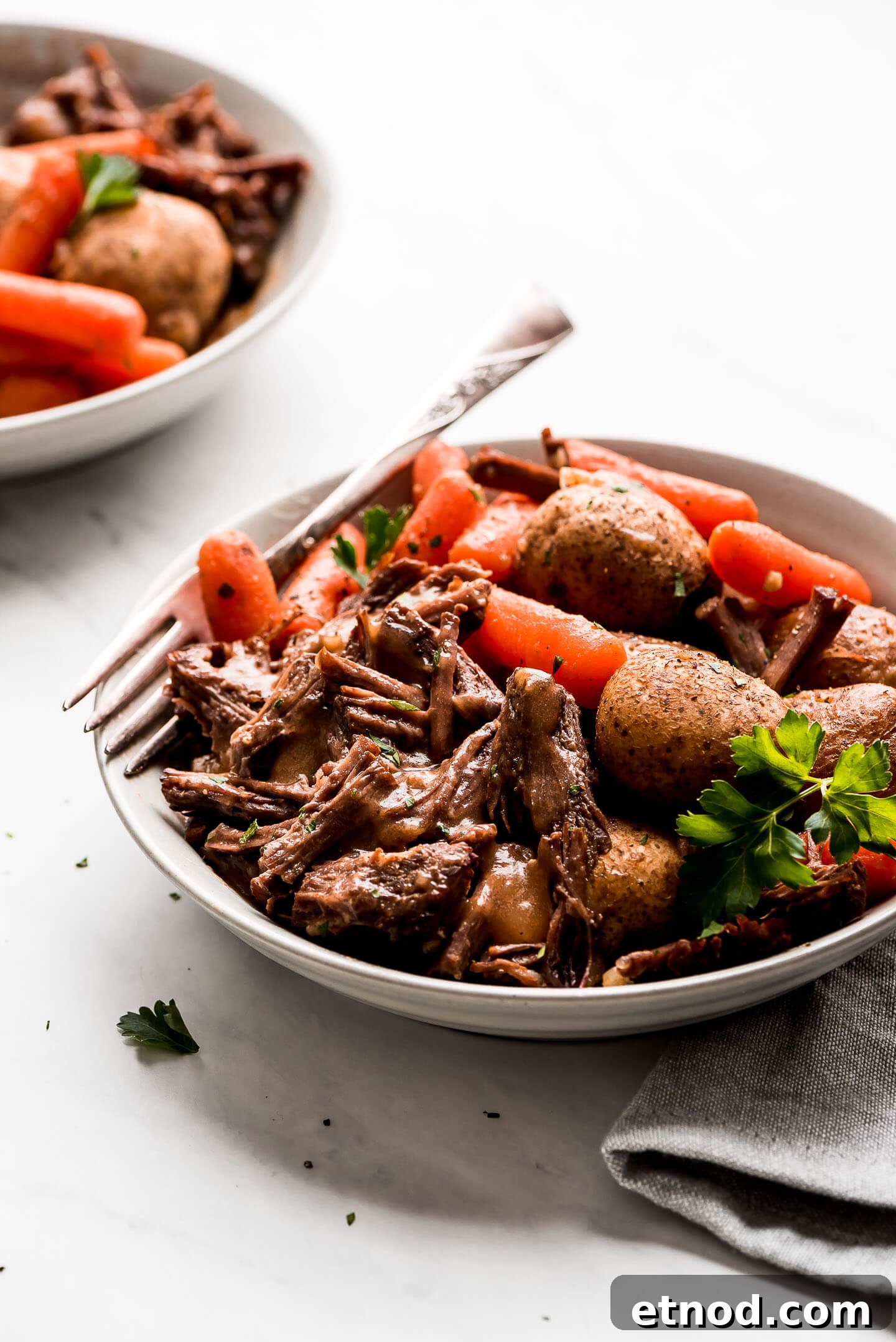 Instant Pot Pot Roast in a bowl with baby carrots, baby yukon potatoes, and gravy.
