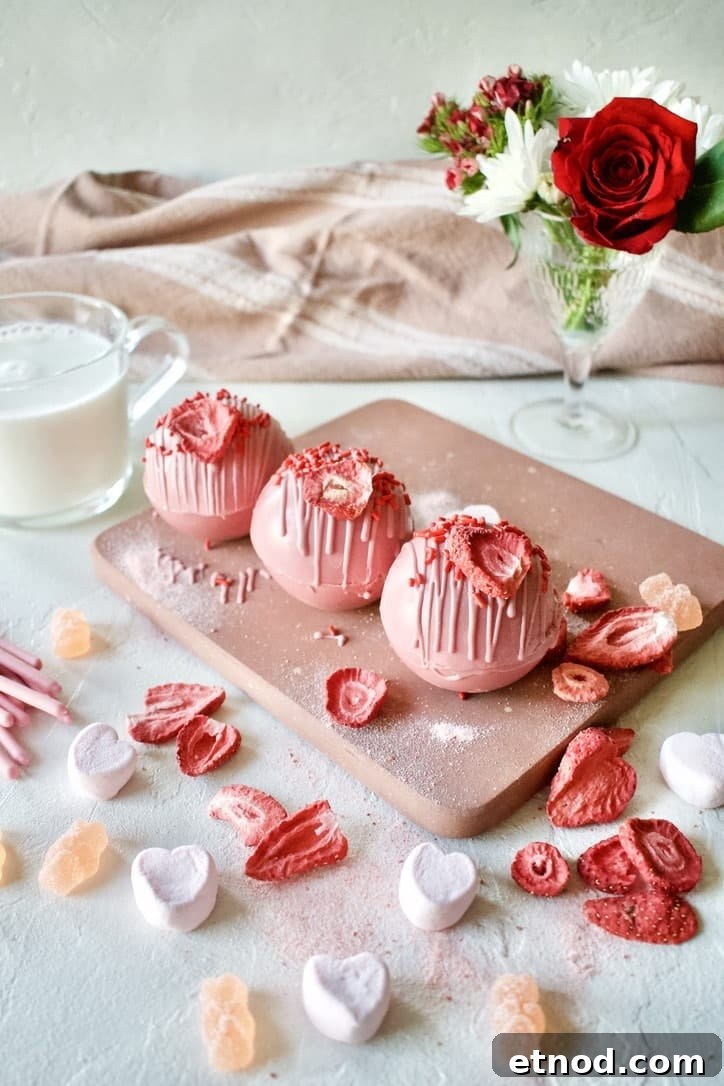 Pink Hot Chocolate Bombs ready to be enjoyed and a warm mug of milk in the back.