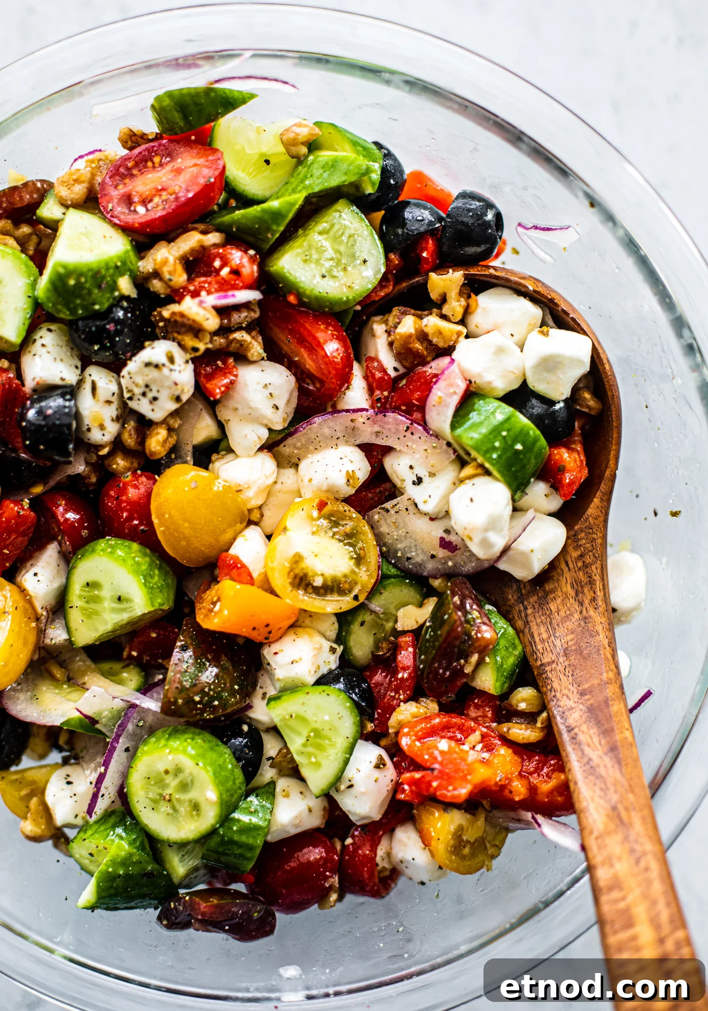 Crisp Greek Cucumber and Tomato Salad Recipe 2 Glass serving bowl of Greek Cucumber Tomato Salad with a wooden serving spoon.