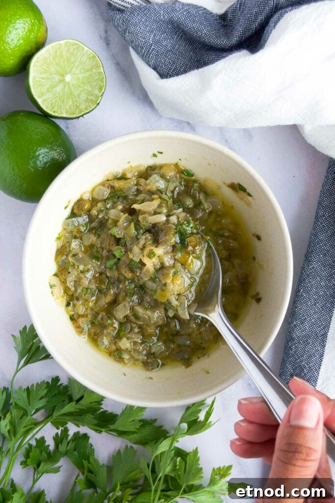 a hand stirs a spoon into a bowl of caper sauce for salmon