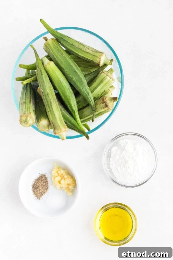 Crispy Air-Fried Okra Recipe for Perfectly Tender Bites 3 Uncooked okra, olive oil, garlic, seasonings, and cornstarch, measured in bowls on a white marble table.