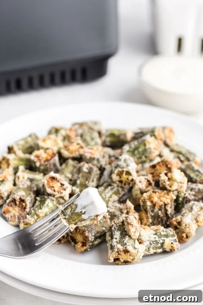 Crispy Air-Fried Okra Recipe for Perfectly Tender Bites 9 Golden okra pieces on a white plate with one piece dipped in ranch dressing on a fork.