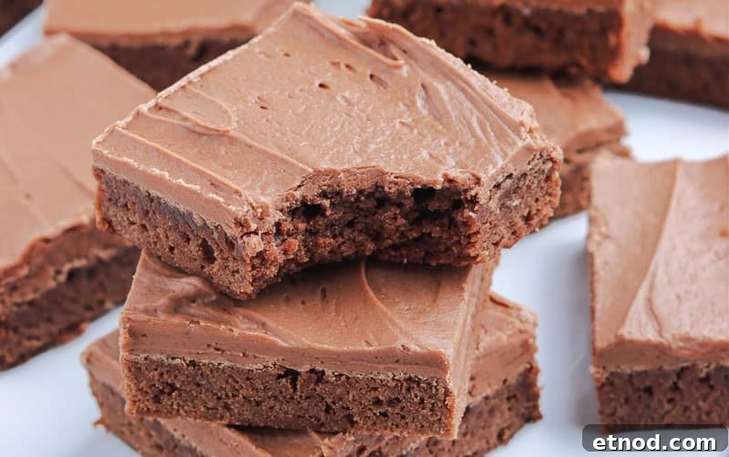 31 Forgotten Grandma Potluck Recipes Worth Bringing Back 2 A pile of neatly cut chocolate-frosted brownies is displayed on a white surface.